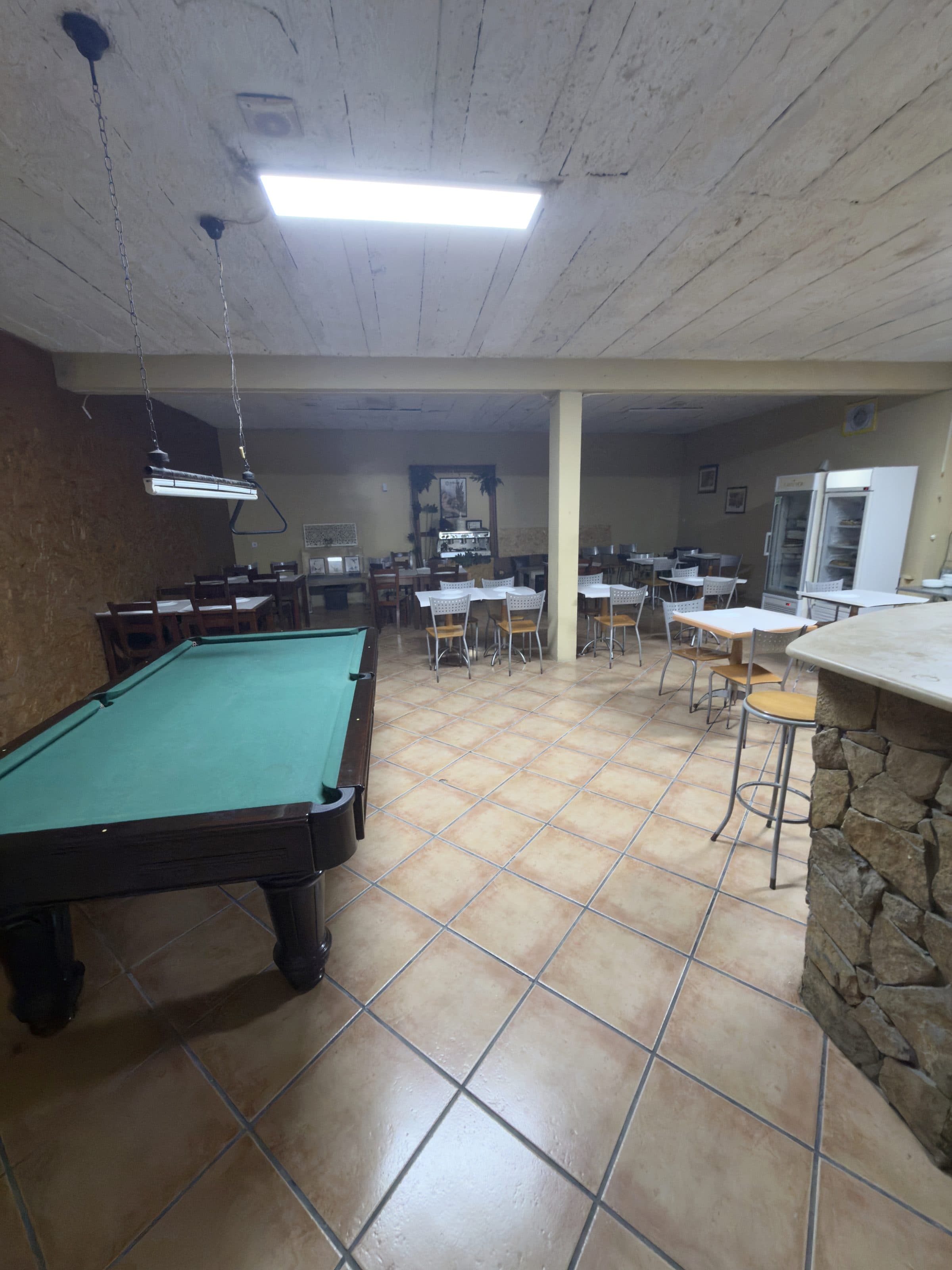 Salão amplo com mesa de bilhar, mesas e vitrina de pastelaria