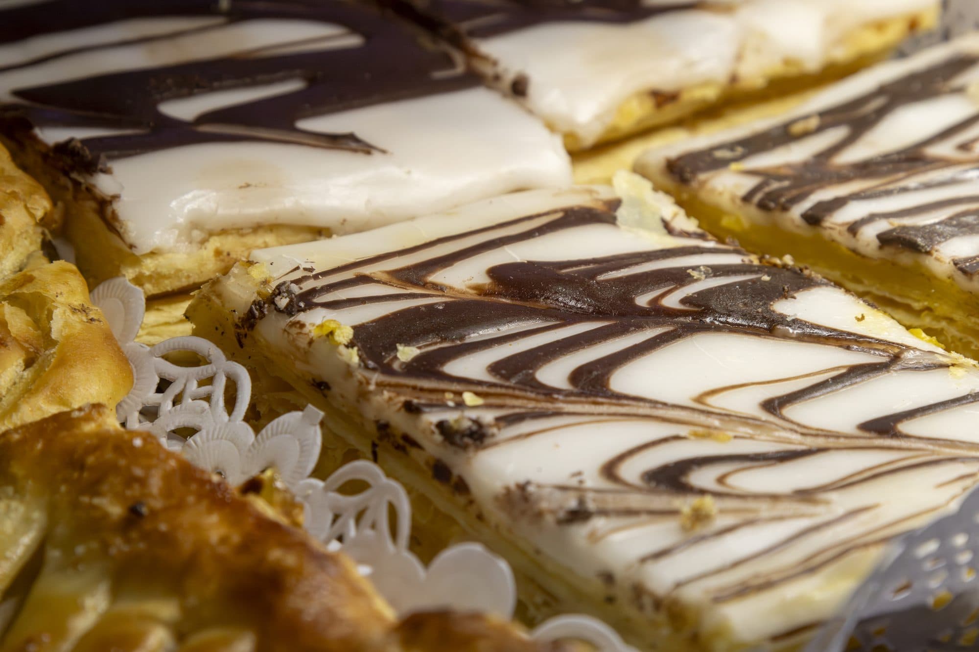 Fatias de folhado com glacé branco e riscas de chocolate, na vitrina
